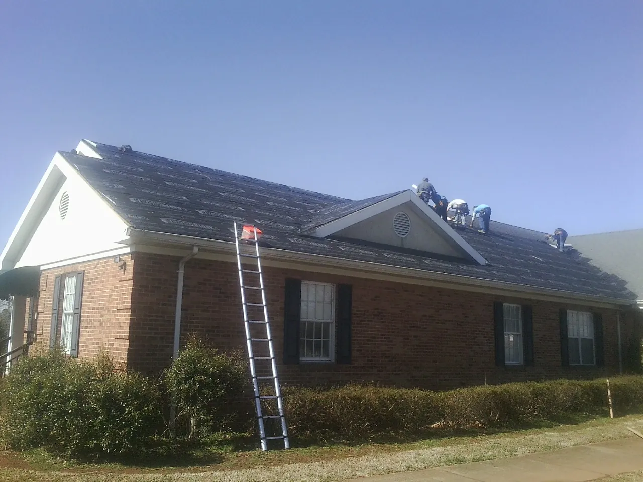 Crew tearing shingles off a brick ranch roof with a ladder set — Emergency Roof Repair work by our crew in Haverhill