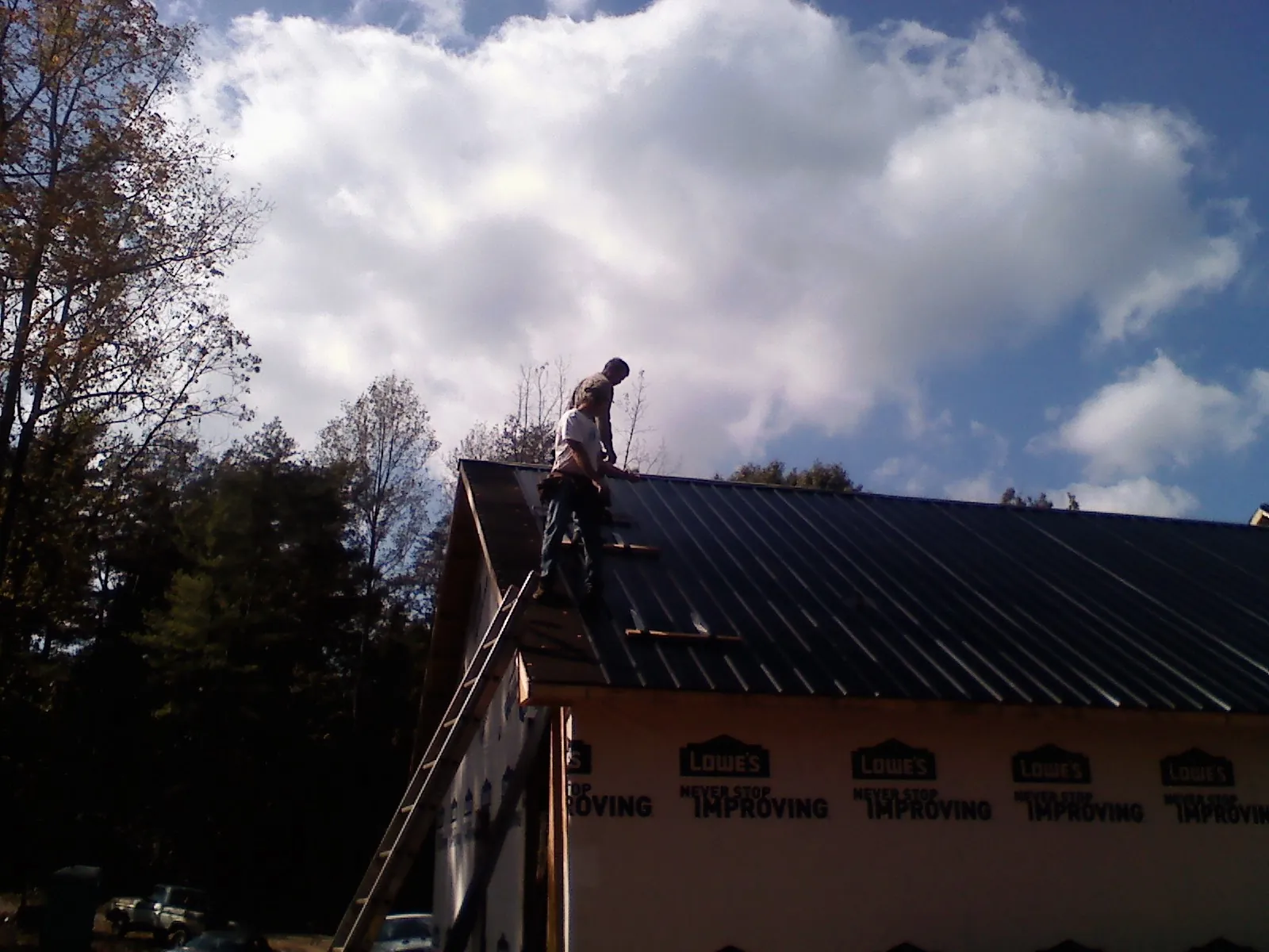 Roofer fastening dark metal panels high against a cloudy sky, from a Roof Inspection job in Haverhill